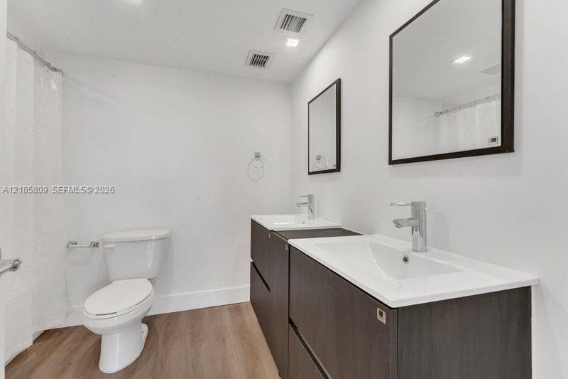 Double vanity featuring dark wood-finish cabinetry, rectangular integrated sinks, chrome fixtures, and wood-finish flooring