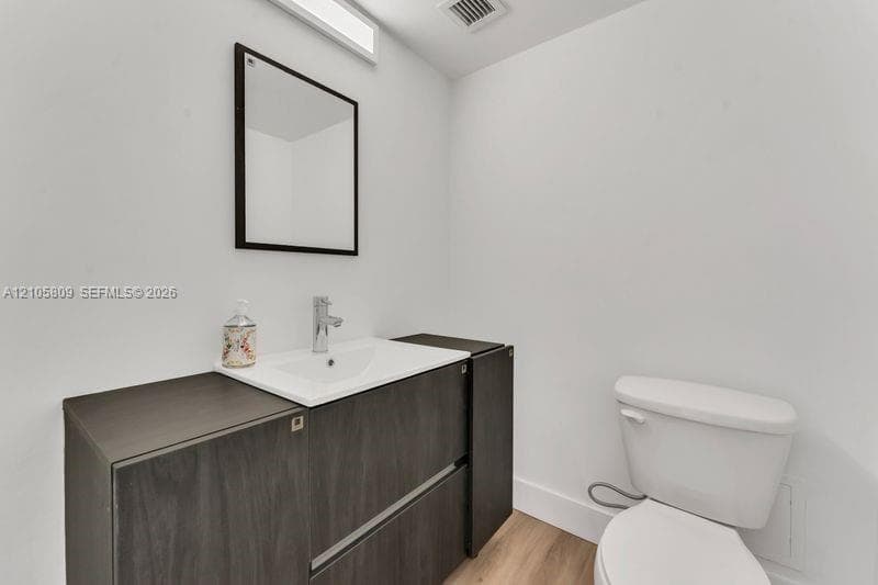 Dark wood-finish vanity with an integrated white sink, chrome faucet, wall-mounted rectangular mirror, and light-toned wood-finish flooring