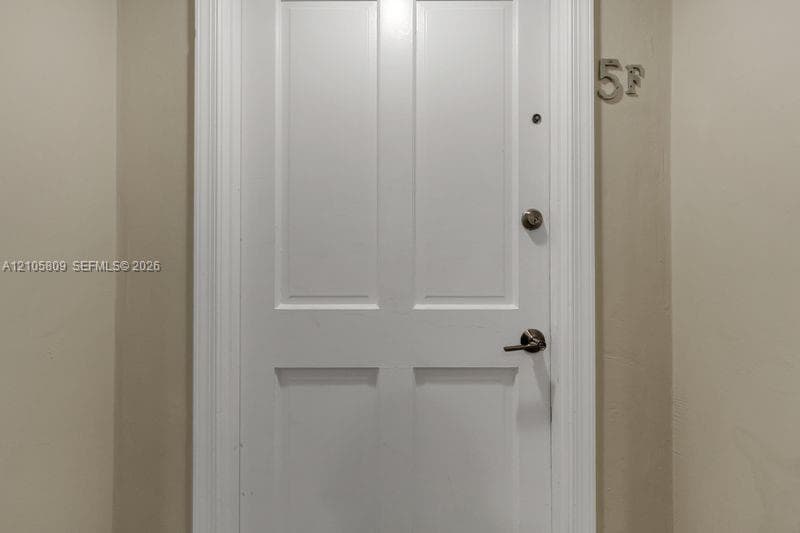 White four-panel door featuring silver-tone lever handle hardware, a security peephole, and integrated metal unit numbering