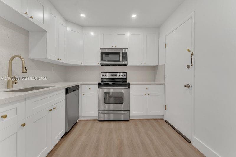 Kitchen featuring white shaker-style cabinetry, quartz countertops, stainless steel appliances, wood-finish flooring, and a high-arch gold-toned faucet