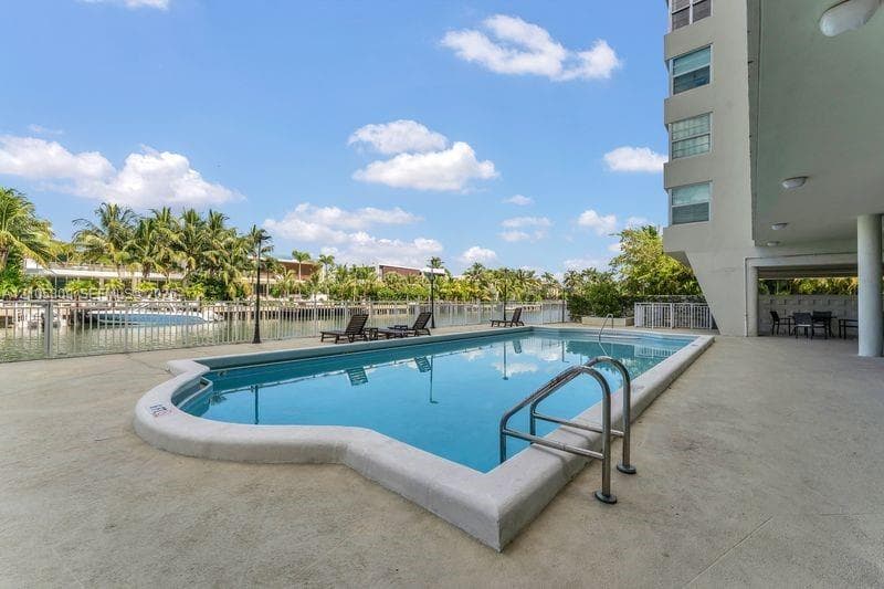 Waterfront swimming pool with concrete decking, metal perimeter fencing, and stainless steel ladder