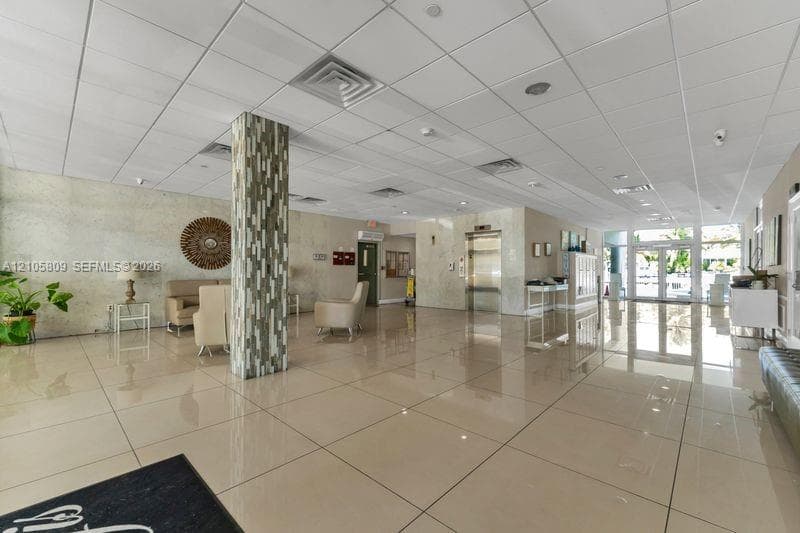 Spacious lobby featuring polished tile flooring, stone-tiled accent pillar, recessed ceiling lighting, and brushed metal elevator doors