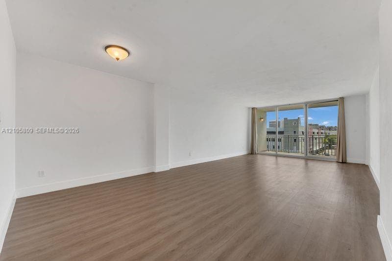 Open floor plan featuring wood-finish flooring, floor-to-ceiling glass doors, and a private balcony with iron railing
