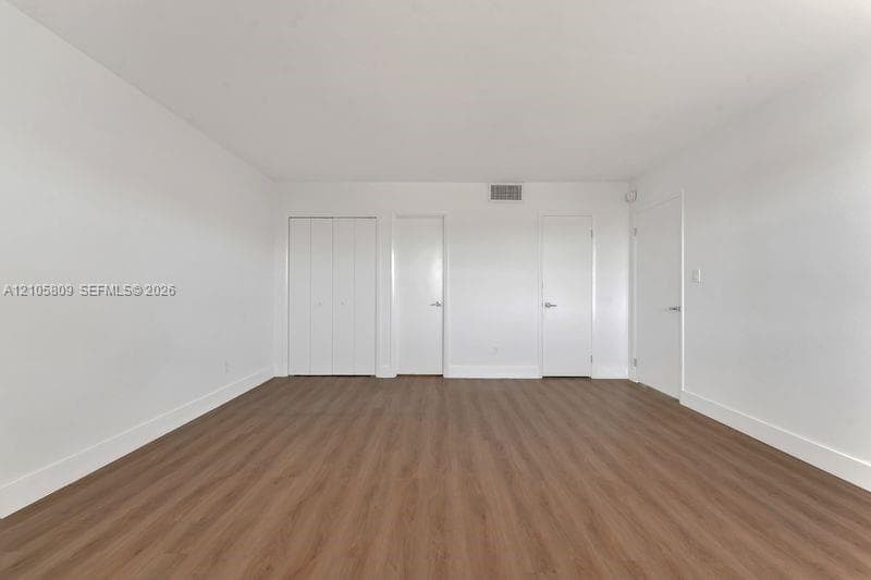 Interior room featuring wood-finish flooring, white walls, and multiple door entries including a double-panel closet