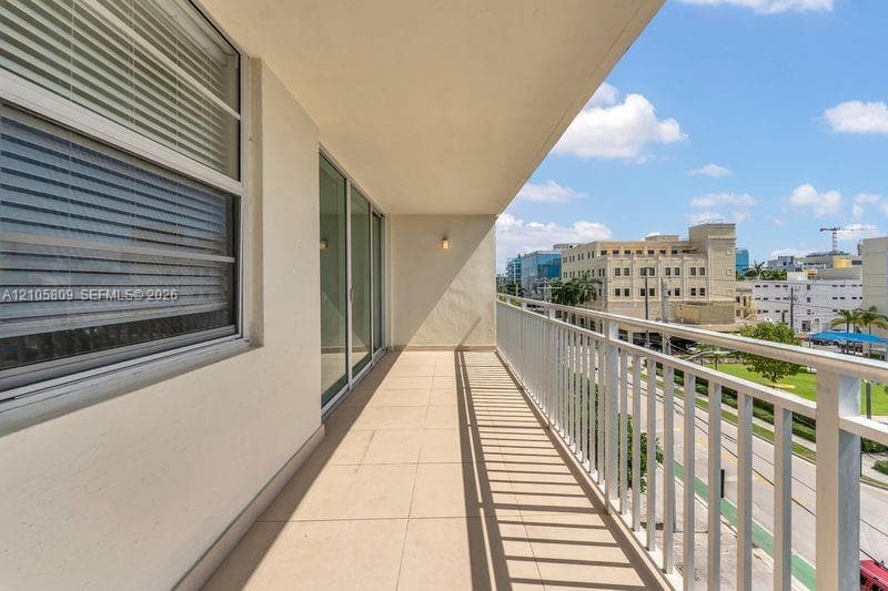 Covered balcony featuring neutral tile flooring, white metal railing, wall-mounted exterior lighting, and floor-to-ceiling sliding glass doors