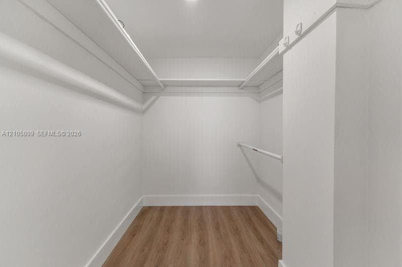 Walk-in closet featuring white wood shelving, multiple hanging rods, and wood-finish flooring