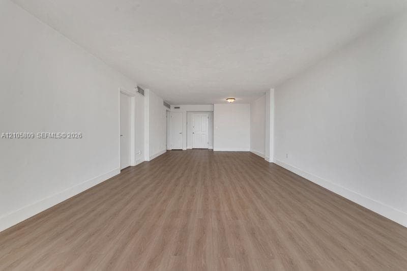 Neutral interior space featuring wood-finish flooring, smooth white walls, and a flush-mount ceiling fixture