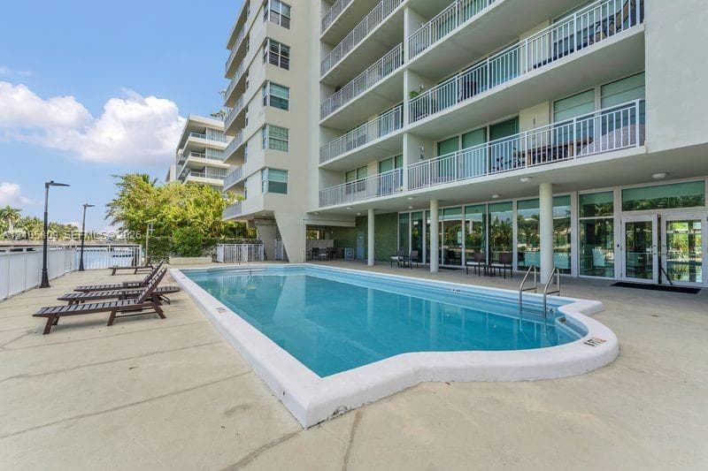 In-ground swimming pool with a concrete deck, multi-story exterior building, and metal balcony railings