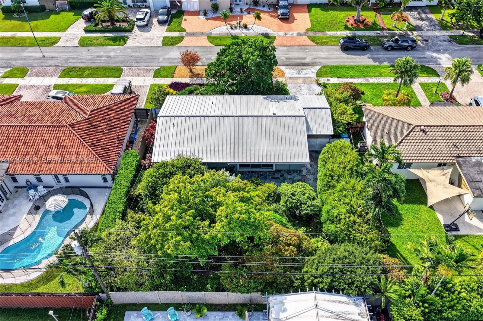 Aerial perspective featuring a metal roof, mature canopy trees, and privacy fencing
