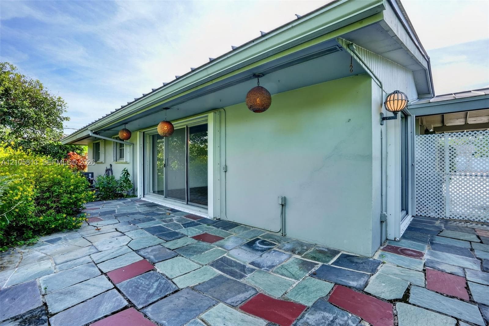 Multicolor natural stone patio featuring sliding glass doors, built-in spherical pendant lighting, and white lattice decorative screening