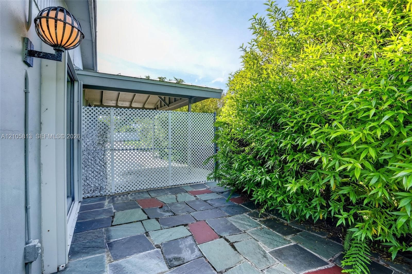 Flagstone patio featuring a white lattice privacy screen, covered exterior overhang, and wall-mounted exterior globe light fixture