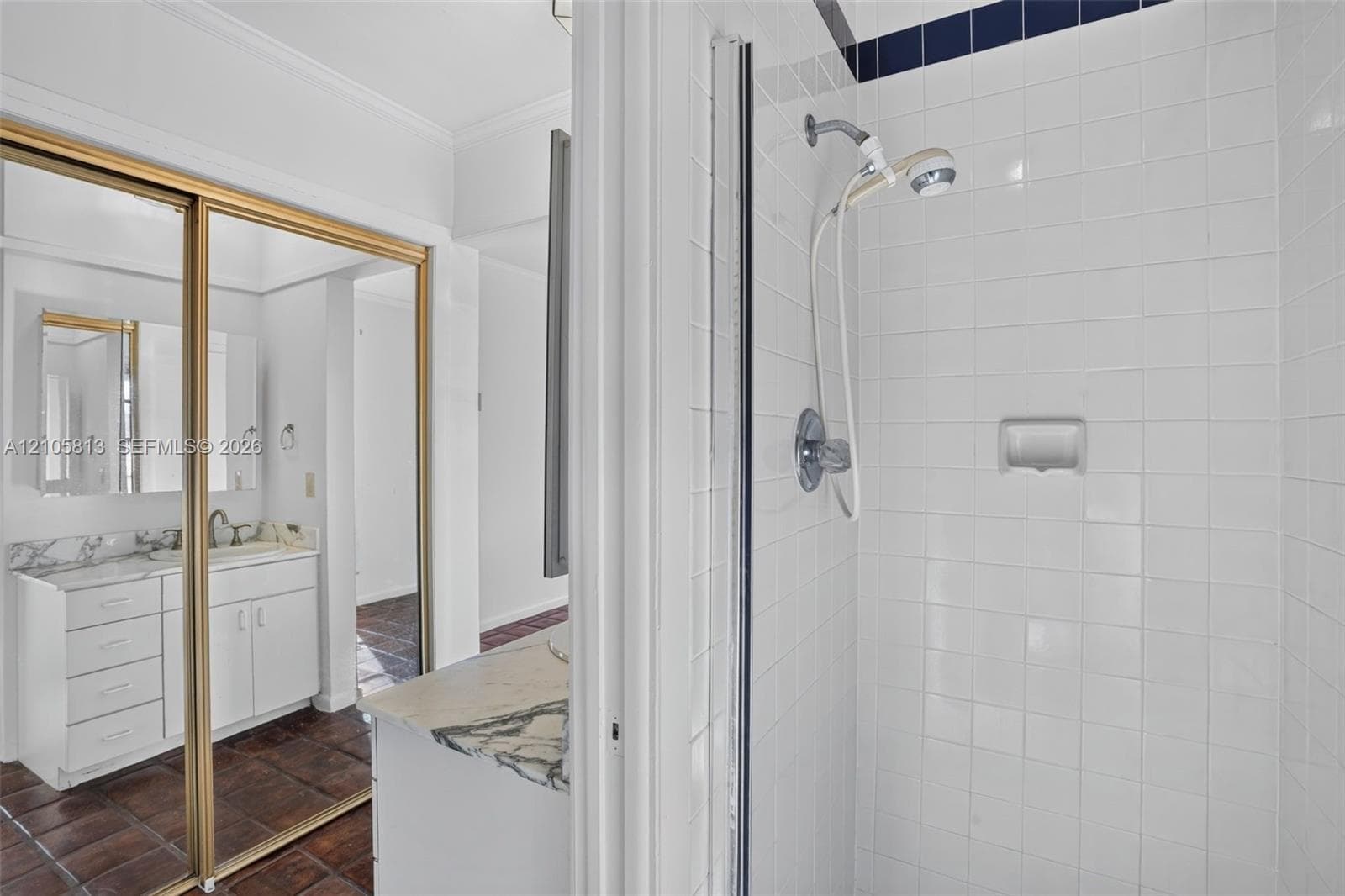 Bathroom featuring a tiled shower enclosure, white cabinetry, vanity with stone-finish countertop, and gold-trimmed sliding mirror doors