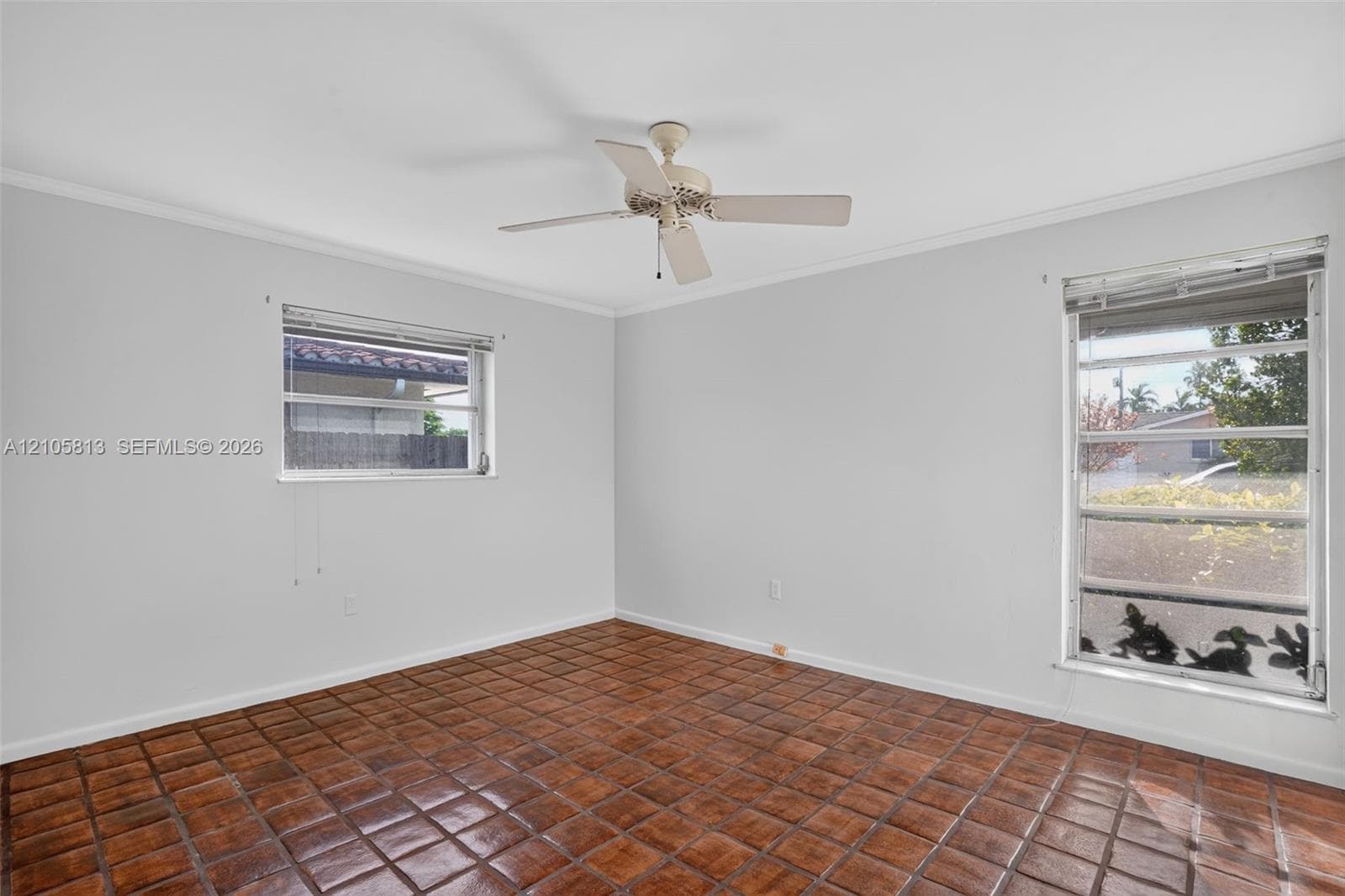 Neutral-toned interior space featuring square clay tile flooring, two multi-pane windows, and a central ceiling fan