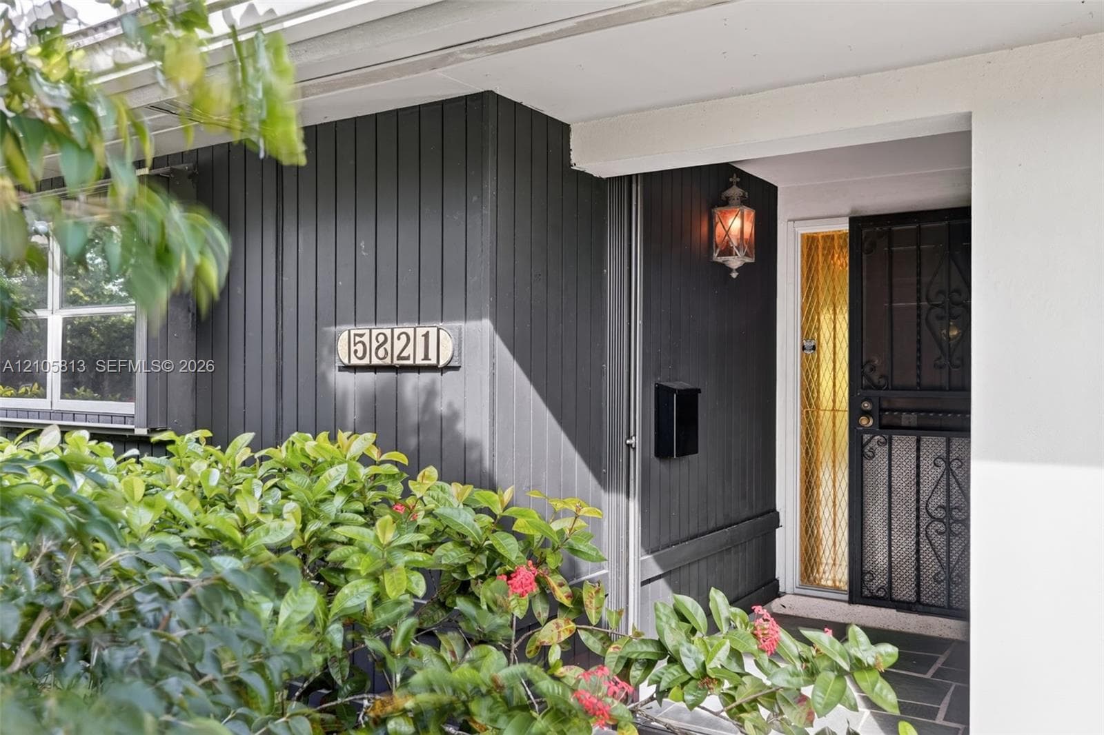Entryway featuring vertical charcoal-toned siding, a decorative wrought-iron screen door, a traditional wall-mounted lantern, and a stone-tiled porch