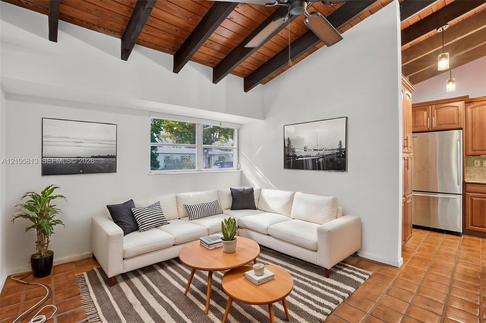 Vaulted ceiling with exposed wooden beams, ceramic tile flooring, and integrated ceiling fan