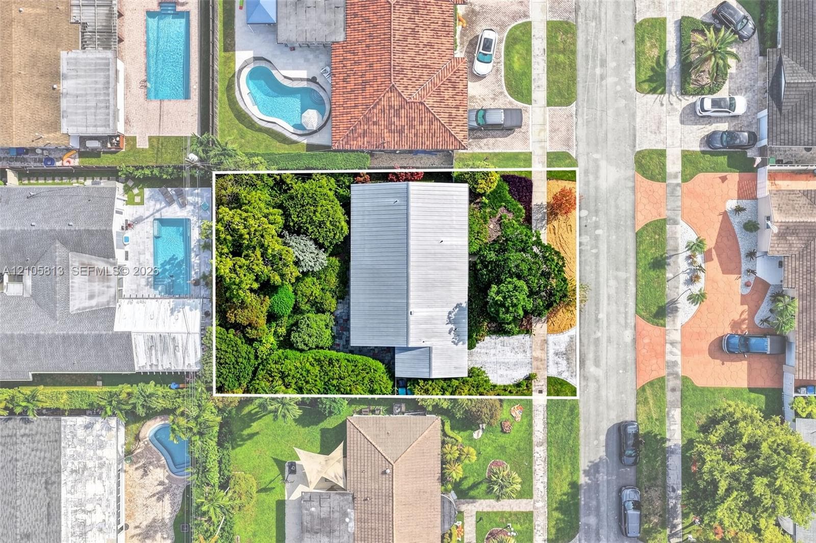 Aerial view of the residential property featuring a metal roof, concrete driveway, and established perimeter landscaping