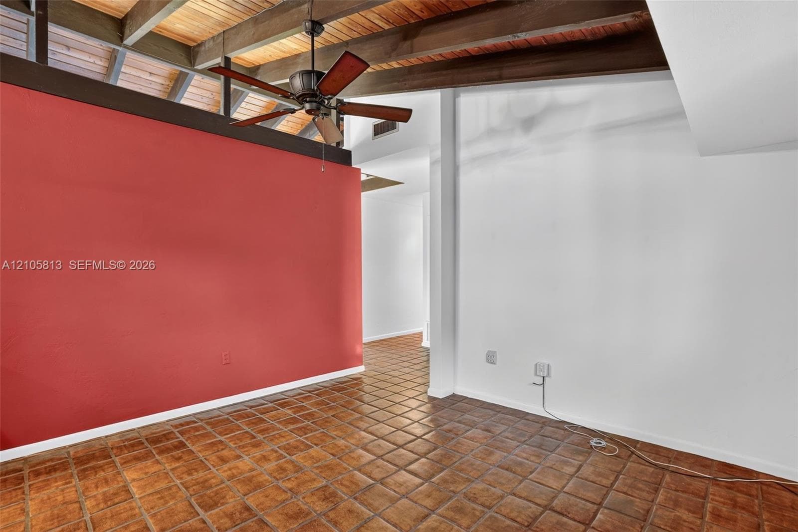 Exposed timber ceiling beams with wood-plank decking, square terra-cotta tile flooring, and integrated ceiling fan