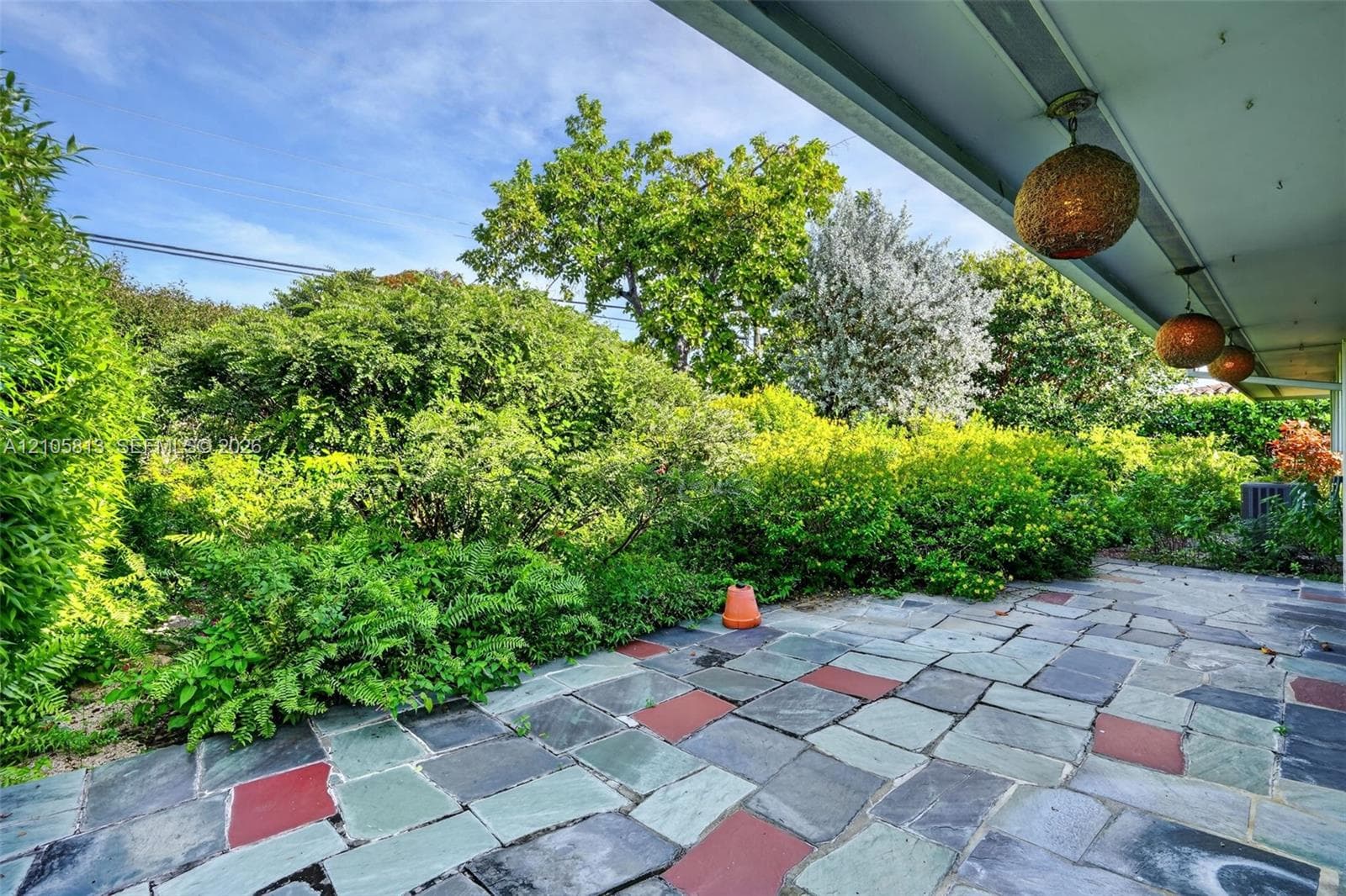 Covered patio featuring multi-toned flagstone paving, integrated spherical pendant lighting, and surrounding mature landscaping