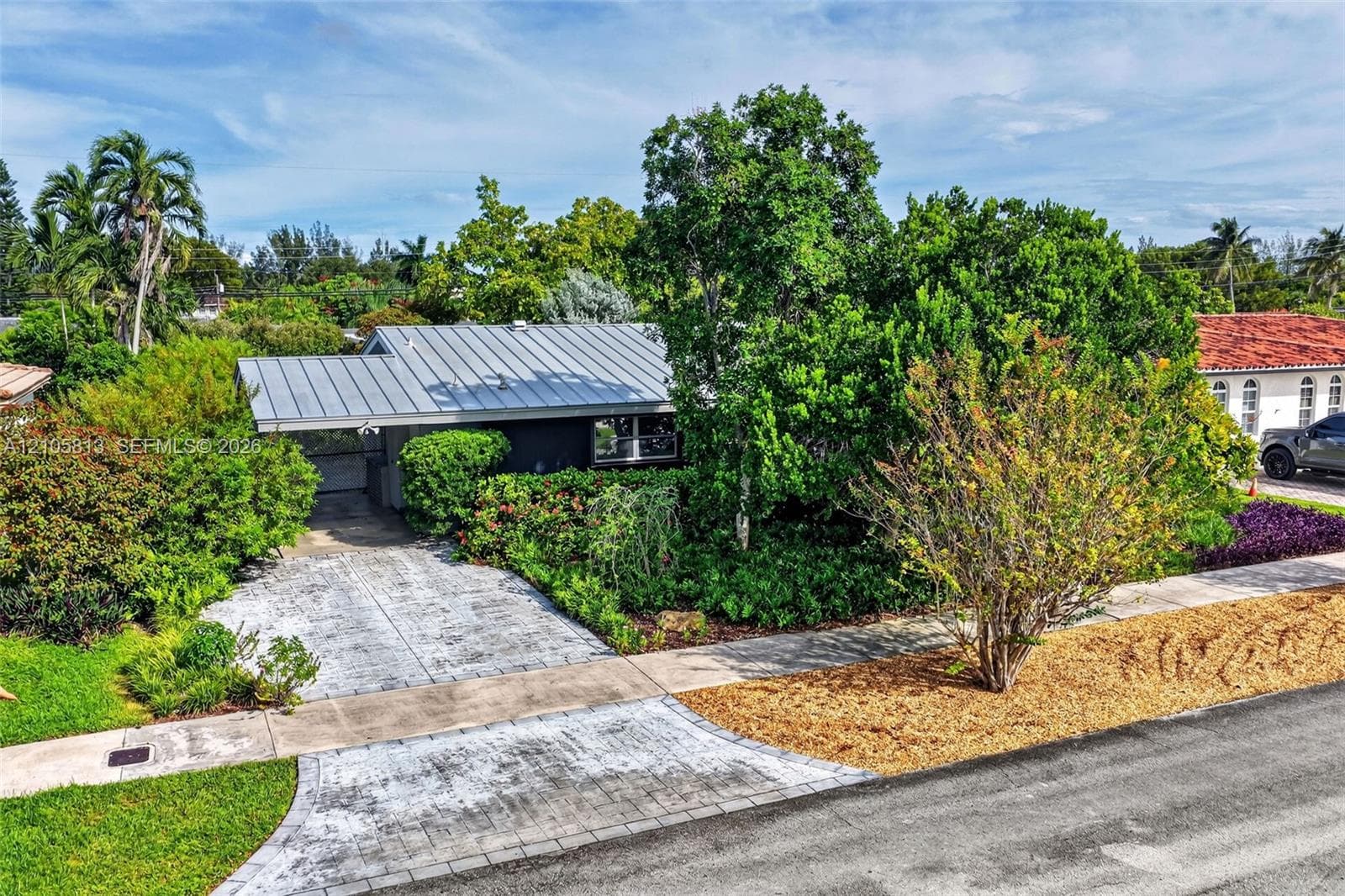 Single-story residence featuring a metal roof, paved driveway, and mature landscaping