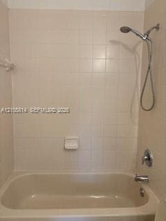 Bathtub and shower combination featuring a ceramic tile surround, integrated soap dish, chrome hand-held shower head, and chrome faucet hardware
