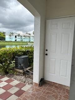 Covered exterior entry featuring stone-tile flooring, a six-panel door, and a dedicated concrete pad for mechanical equipment