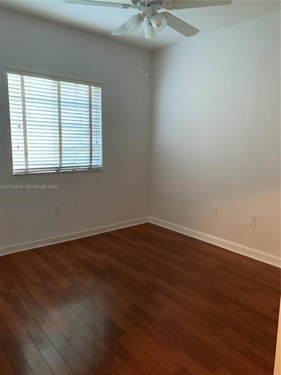 Room interior featuring wood-finish flooring, a multi-light ceiling fan, and window fitted with horizontal blinds