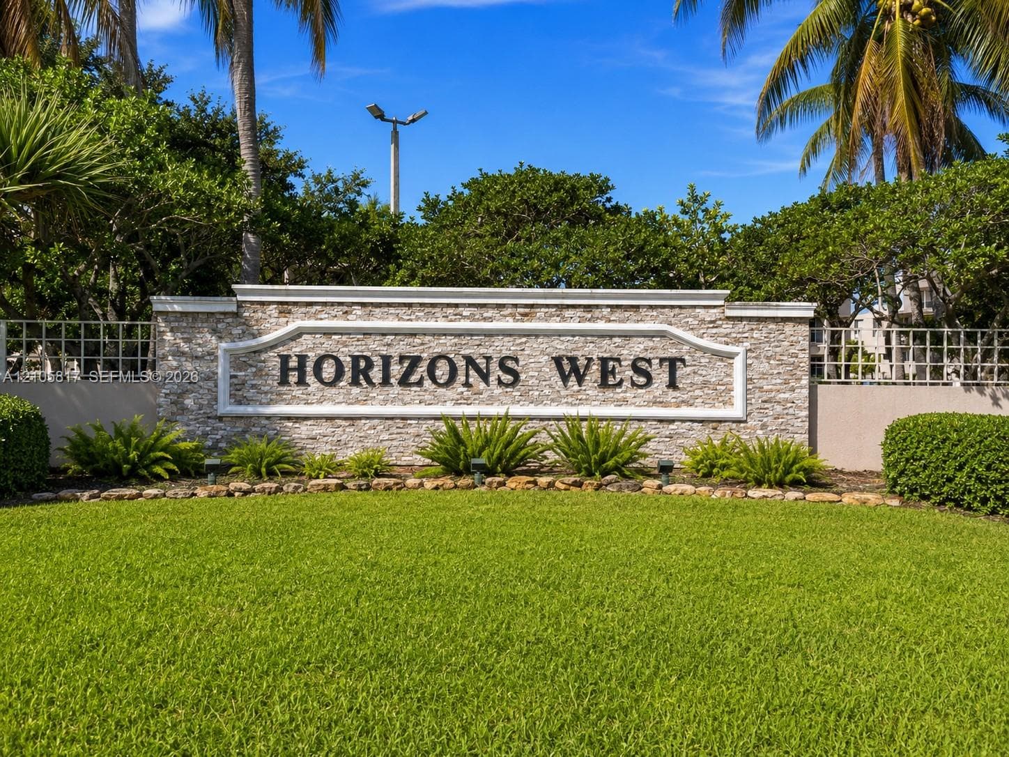 Stacked-stone monument sign featuring dimensional lettering, flanked by concrete perimeter walls and mature tropical landscaping