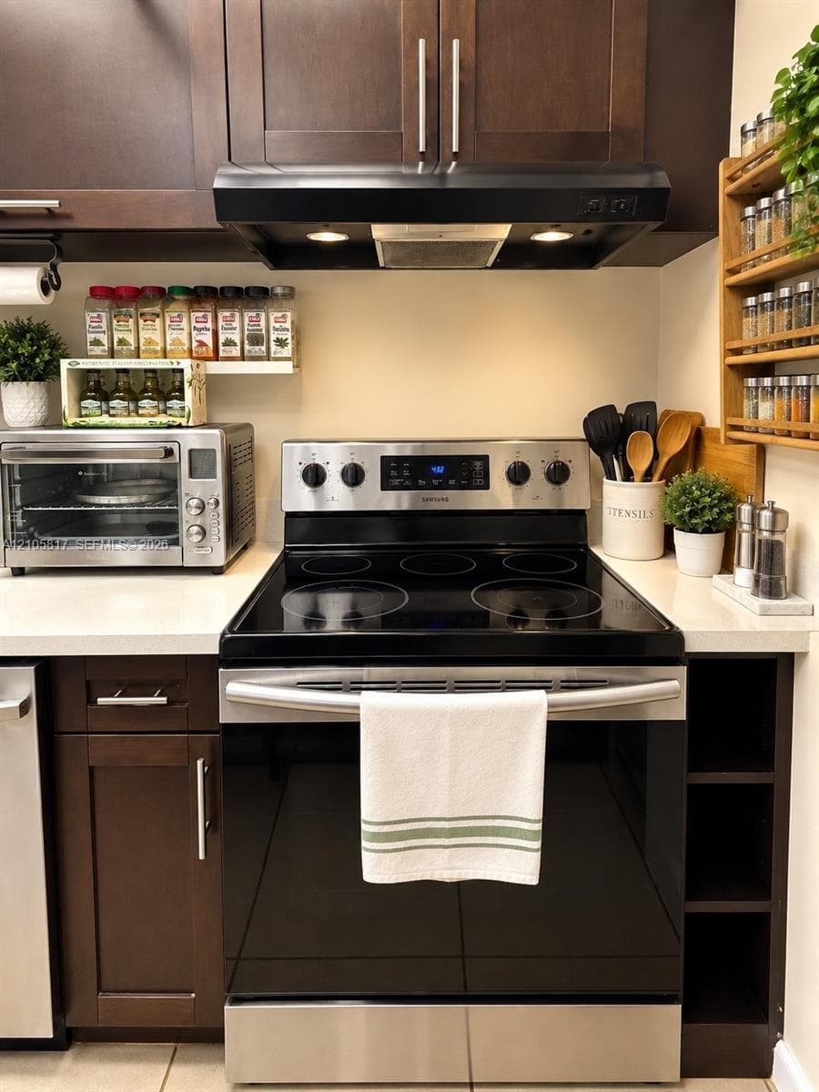 Dark wood cabinetry, stainless steel electric range, matte black range hood with integrated lighting, and solid surface countertops