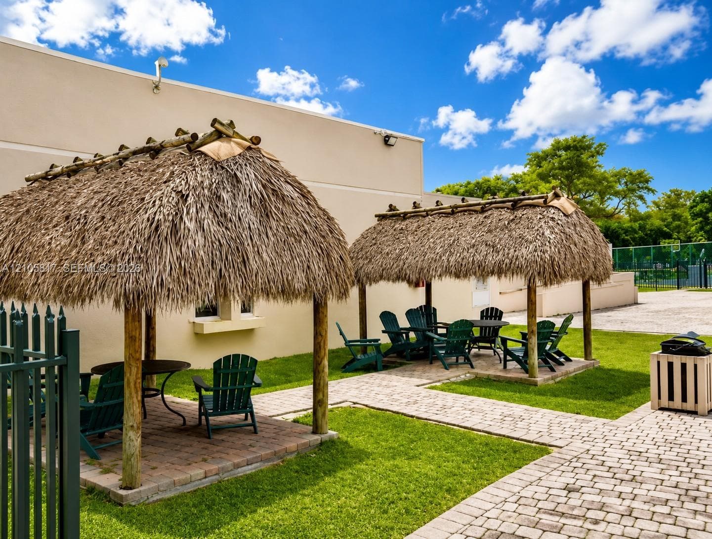 Outdoor area featuring two thatched-roof structures with timber support posts, paver stone flooring, and manicured lawn