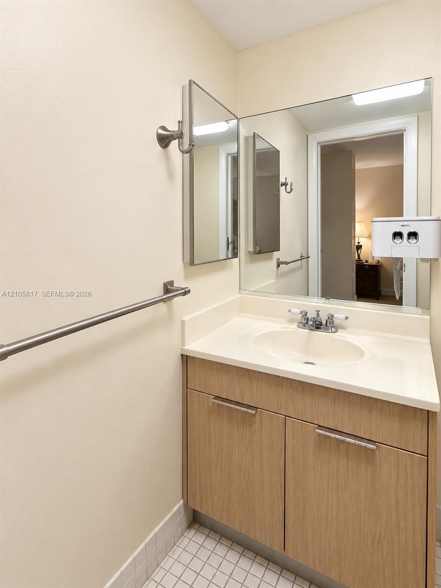 Wood-finish vanity with an integrated basin, large wall-mounted mirror, brushed nickel hardware, and tiled flooring