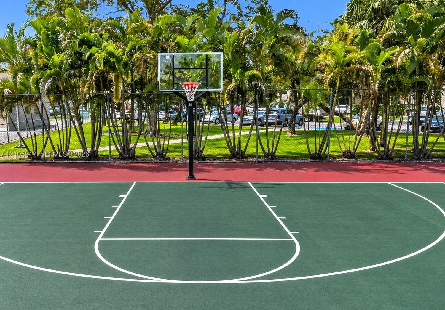 Outdoor basketball court with a green painted surface, red border, and a fixed hoop system