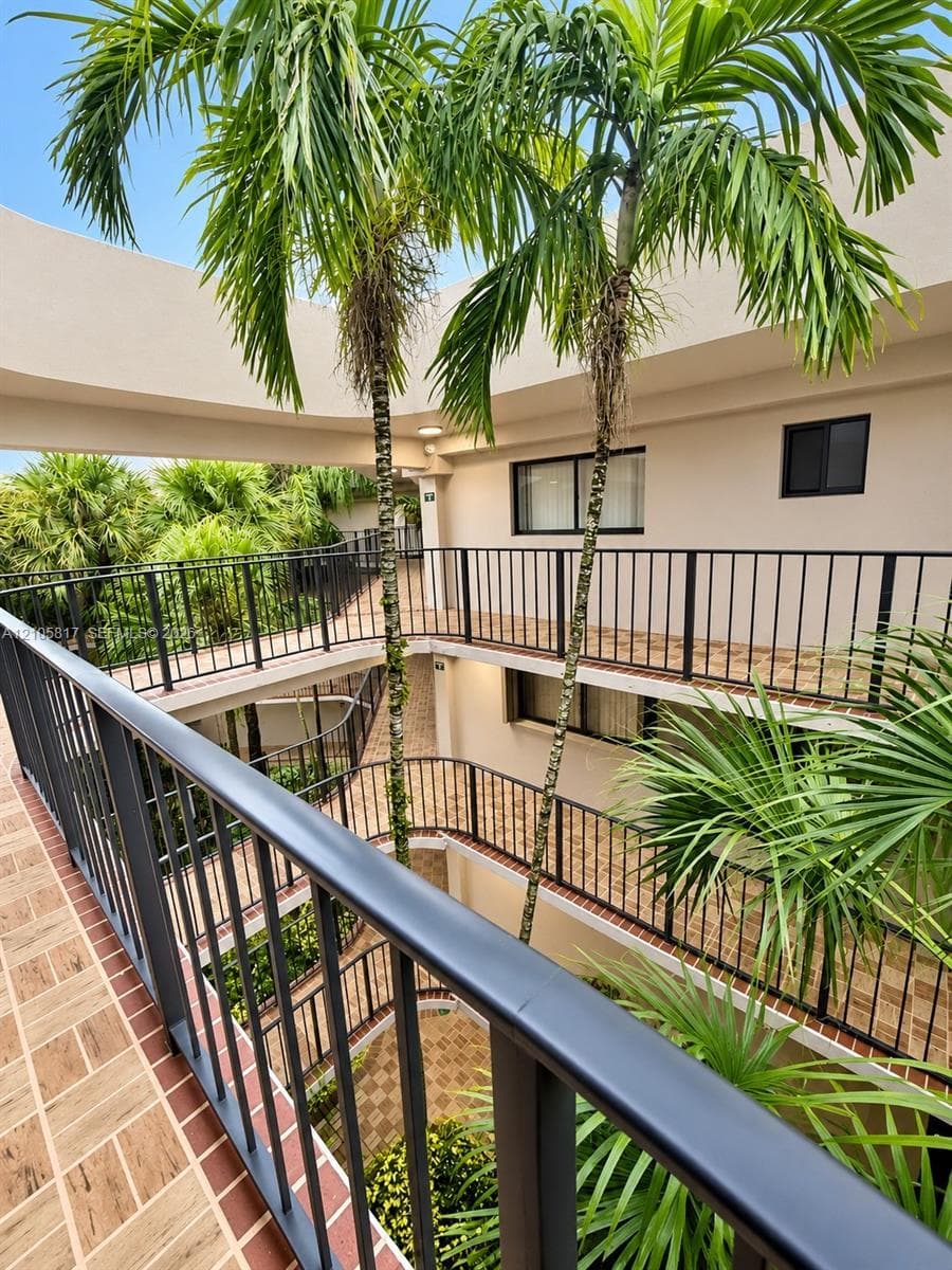 Multi-level exterior corridors featuring black metal railings, tiled flooring, and central mature palm trees