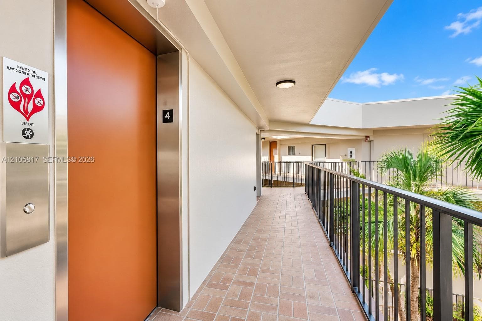 Exterior corridor featuring tile flooring, metal handrail, recessed ceiling lighting, and elevator access