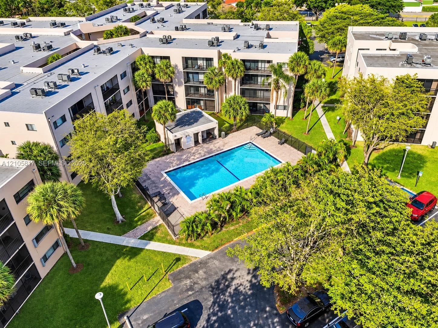 Outdoor swimming pool with paved deck, multi-story exterior architecture, and surrounding landscaped grounds with mature palm trees