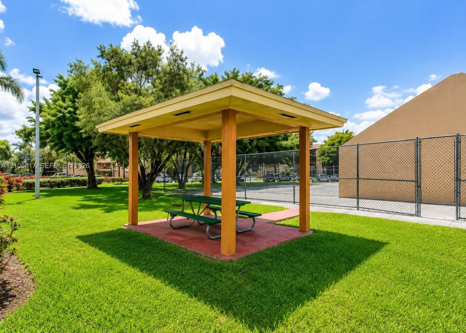 Outdoor pavilion featuring a covered structure with wooden support posts, a paved foundation, and surrounding manicured lawn area