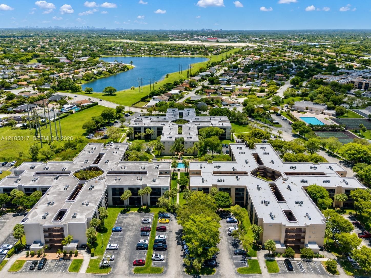 Aerial perspective of a multi-story residential complex featuring designated surface parking, expansive landscaped grounds, and integrated swimming pools