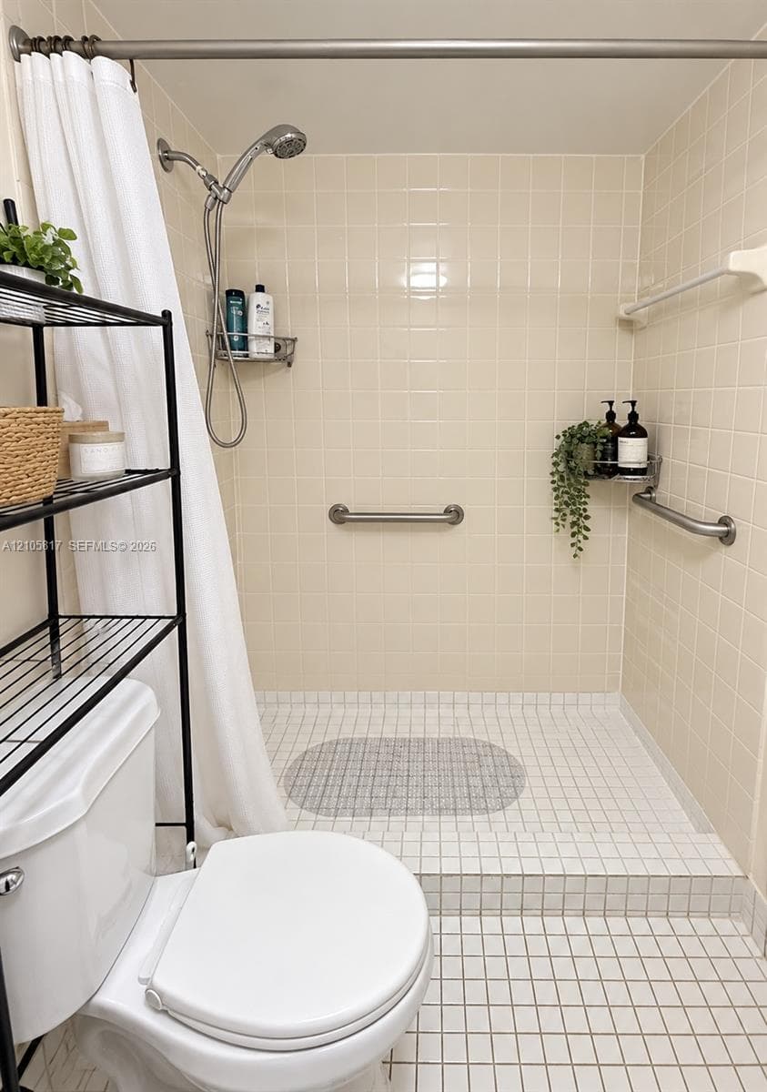 Walk-in shower featuring tiled wall surround, square floor tiling, adjustable handheld showerhead, metal safety grab bars, and mounted storage shelving