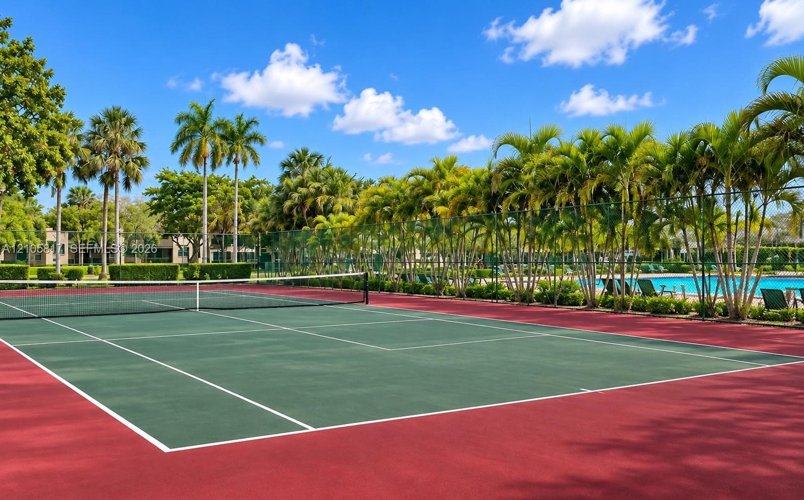 Tennis court featuring a multi-colored hard surface, perimeter fencing, and mature palm tree landscaping