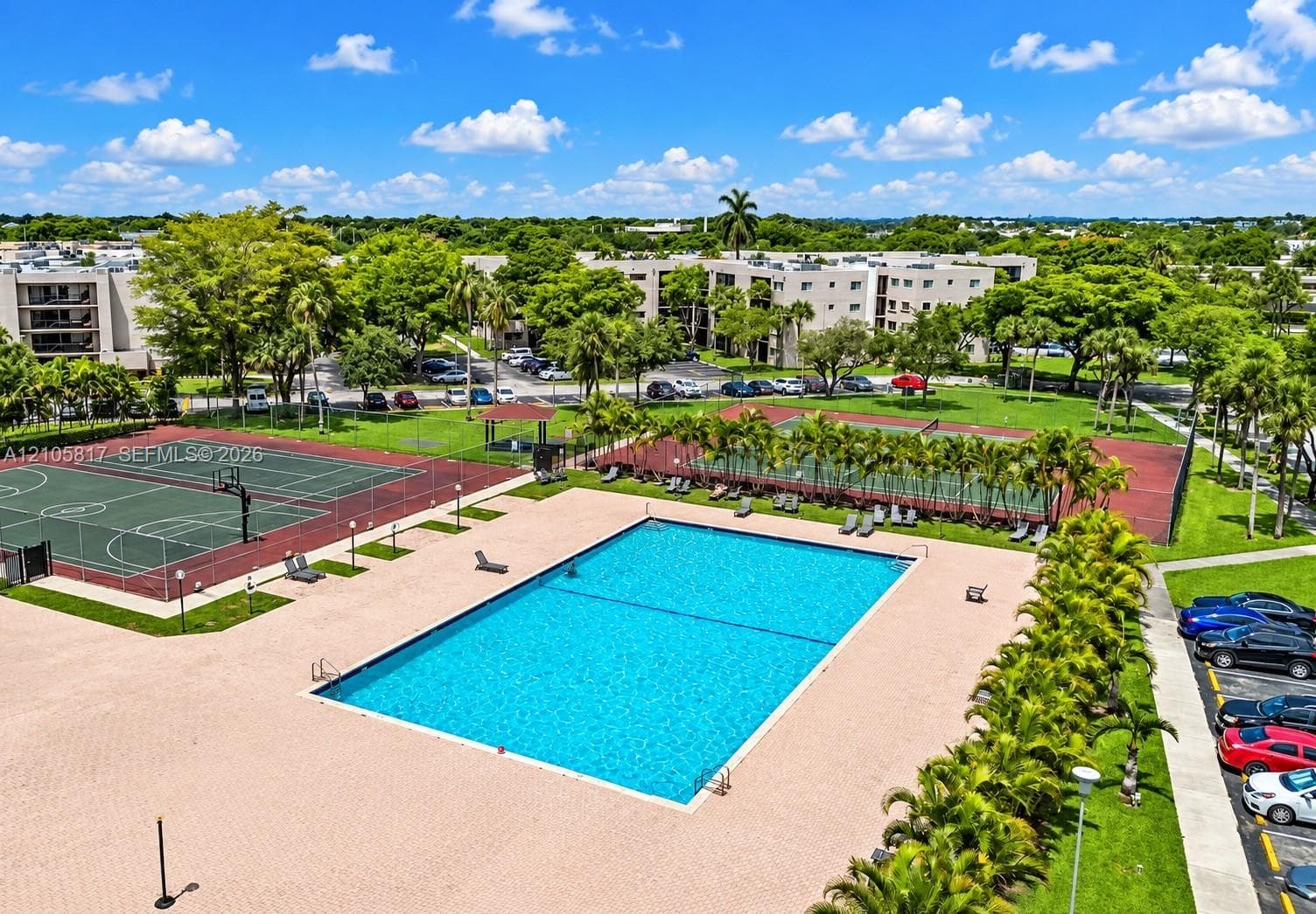 Rectangular swimming pool surrounded by a paved deck, tennis courts, basketball court, and established landscaping