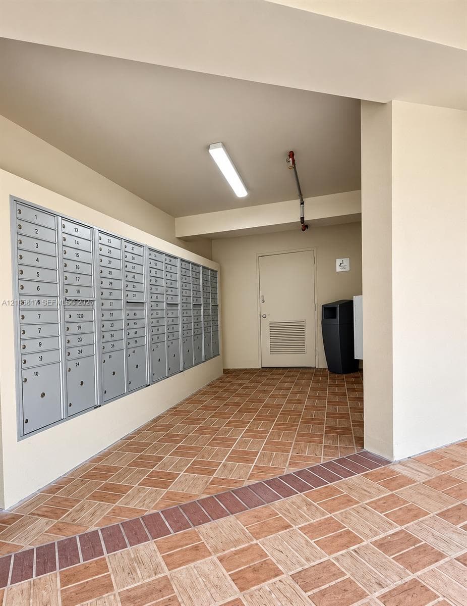 Covered mail center featuring a multi-unit metallic postal station, tile flooring with a brick-style border, and overhead surface-mounted lighting