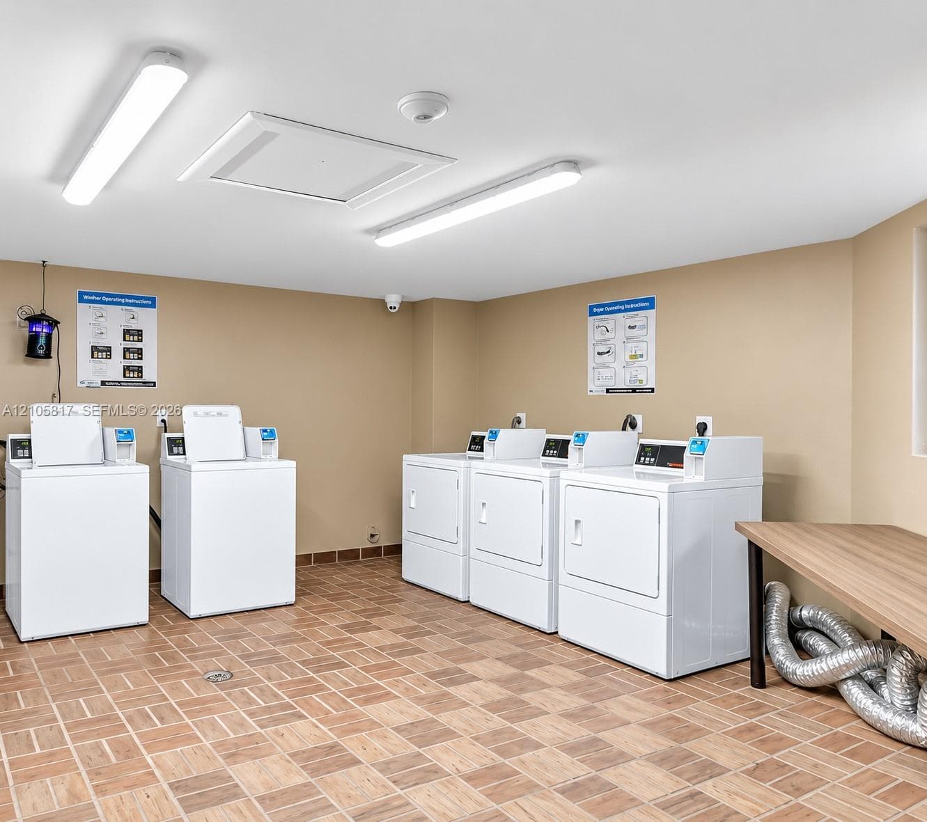 Laundry facility featuring tile flooring, linear LED lighting, and multi-unit laundry appliances with a built-in folding counter