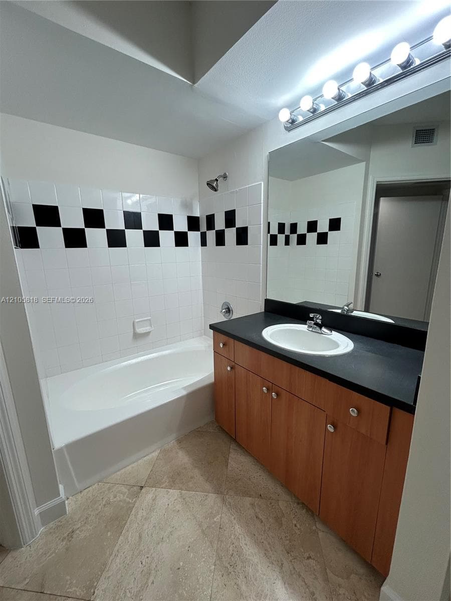 Bathroom featuring a vanity with wood-finish cabinetry, a dark countertop, an integrated oval sink, and a large wall-mounted mirror