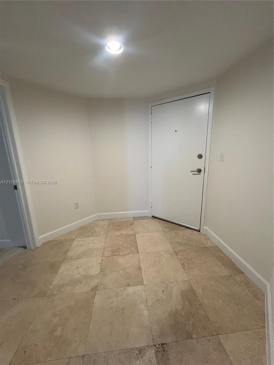 Neutral-toned tile flooring, solid-core white door with polished metal hardware, and recessed ceiling lighting