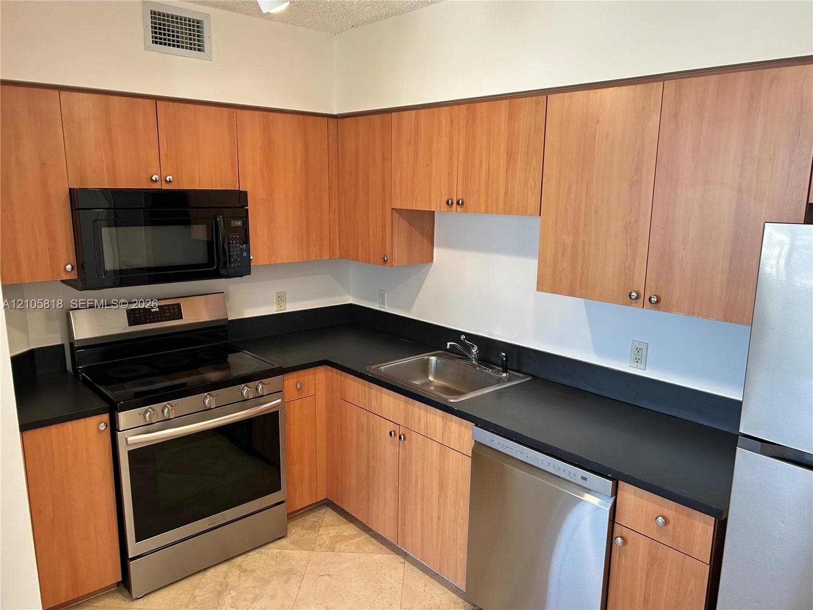 Kitchen featuring flat-panel wood-finish cabinetry, solid surface countertops, stainless steel appliance suite, and a drop-in stainless steel sink
