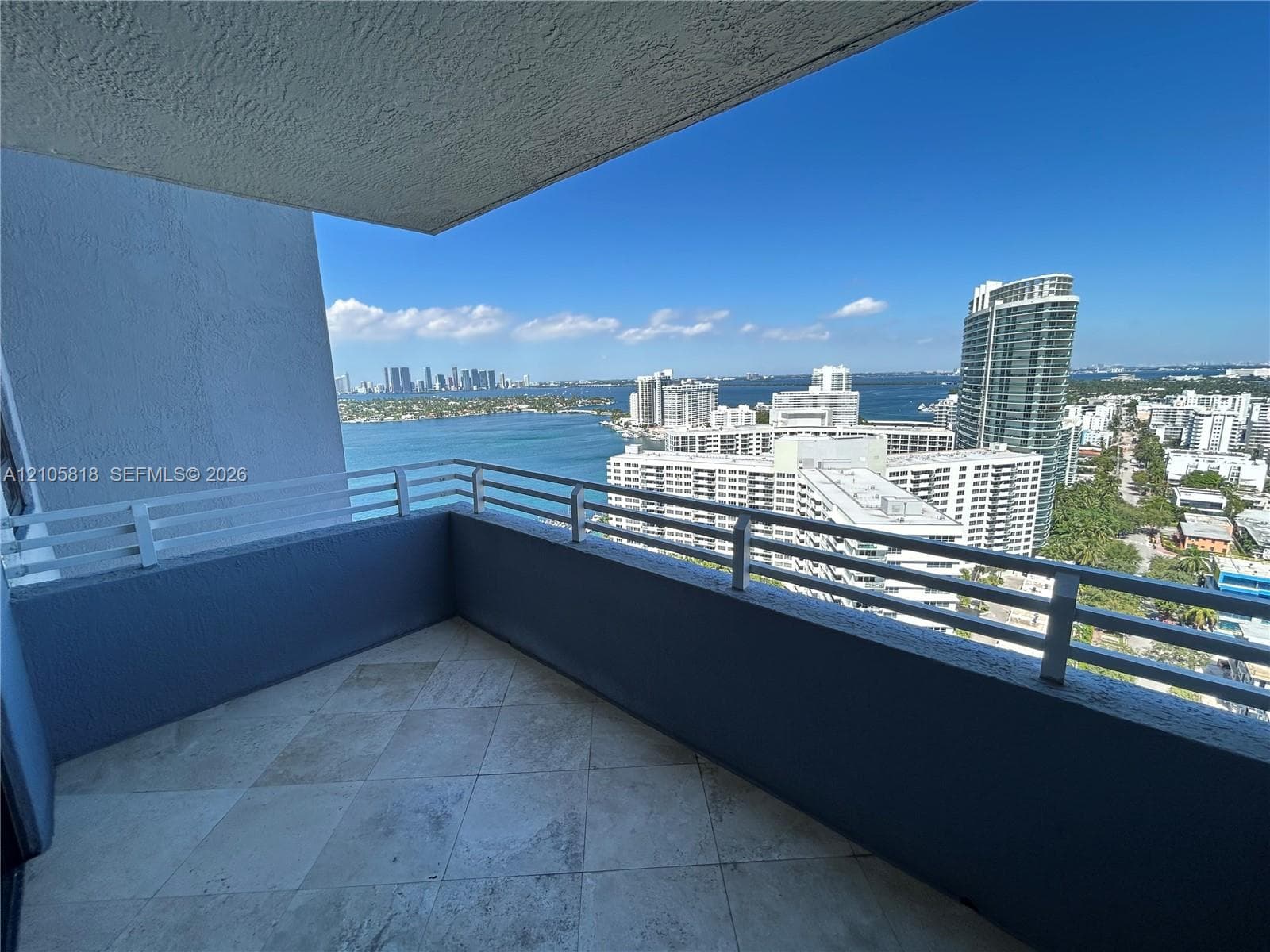 Covered balcony featuring stone tile flooring and white metal railings with water and skyline scenery