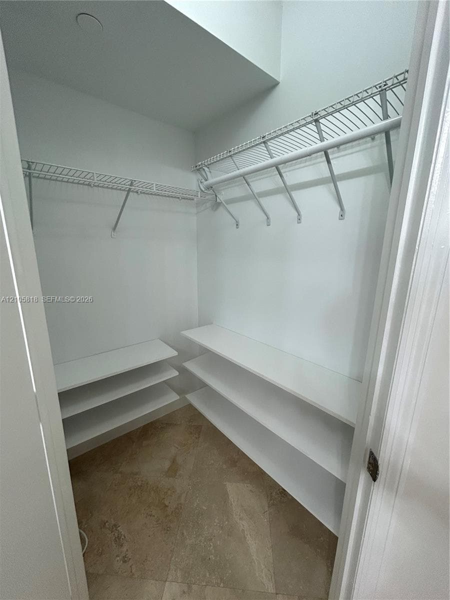 Storage space featuring white tiered shelving, wire rack organizers, and tile flooring