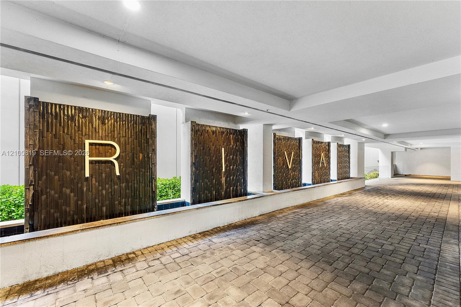 Covered arrival area featuring stone-paver flooring, recessed lighting, and a series of vertical water features with integrated architectural lettering