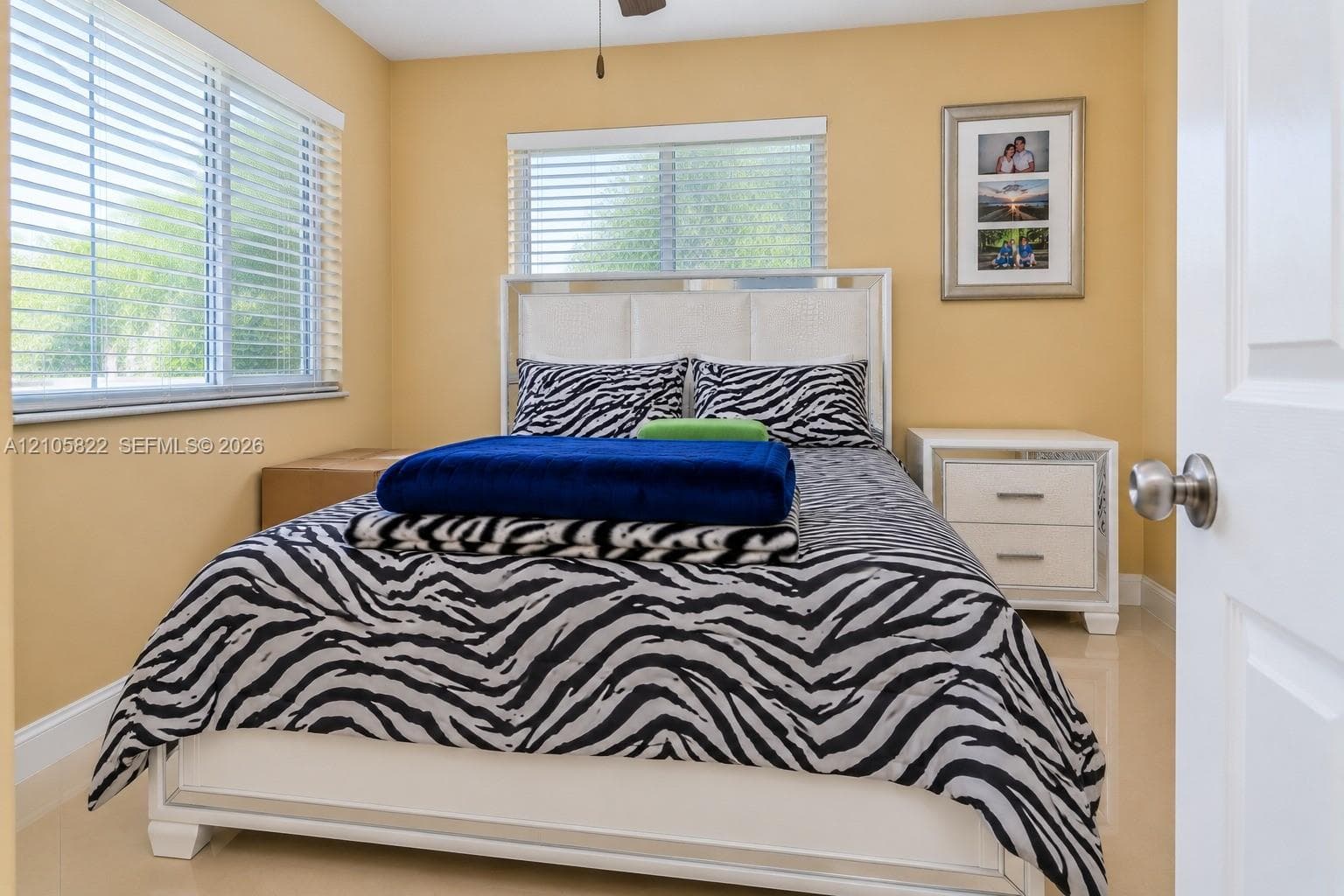 Neutral-toned interior featuring large-format tile flooring, dual horizontal windows with fitted blinds, and a ceiling-mounted fan