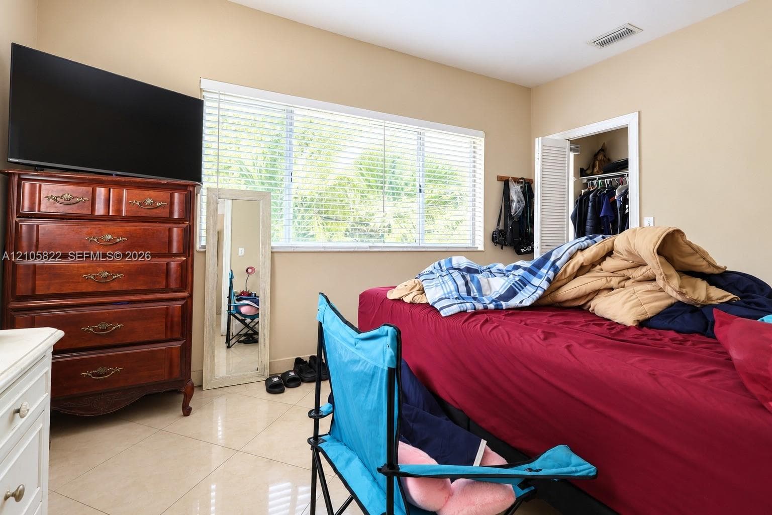 Neutral-tone walls, tile flooring, large horizontal window with fitted blinds, and closet with louvered bifold doors