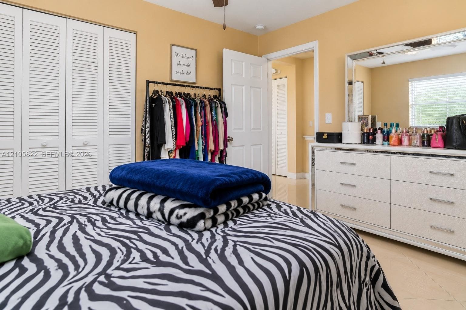 Bedroom featuring large-format tile flooring, ceiling fan, and white louvered-panel closet doors